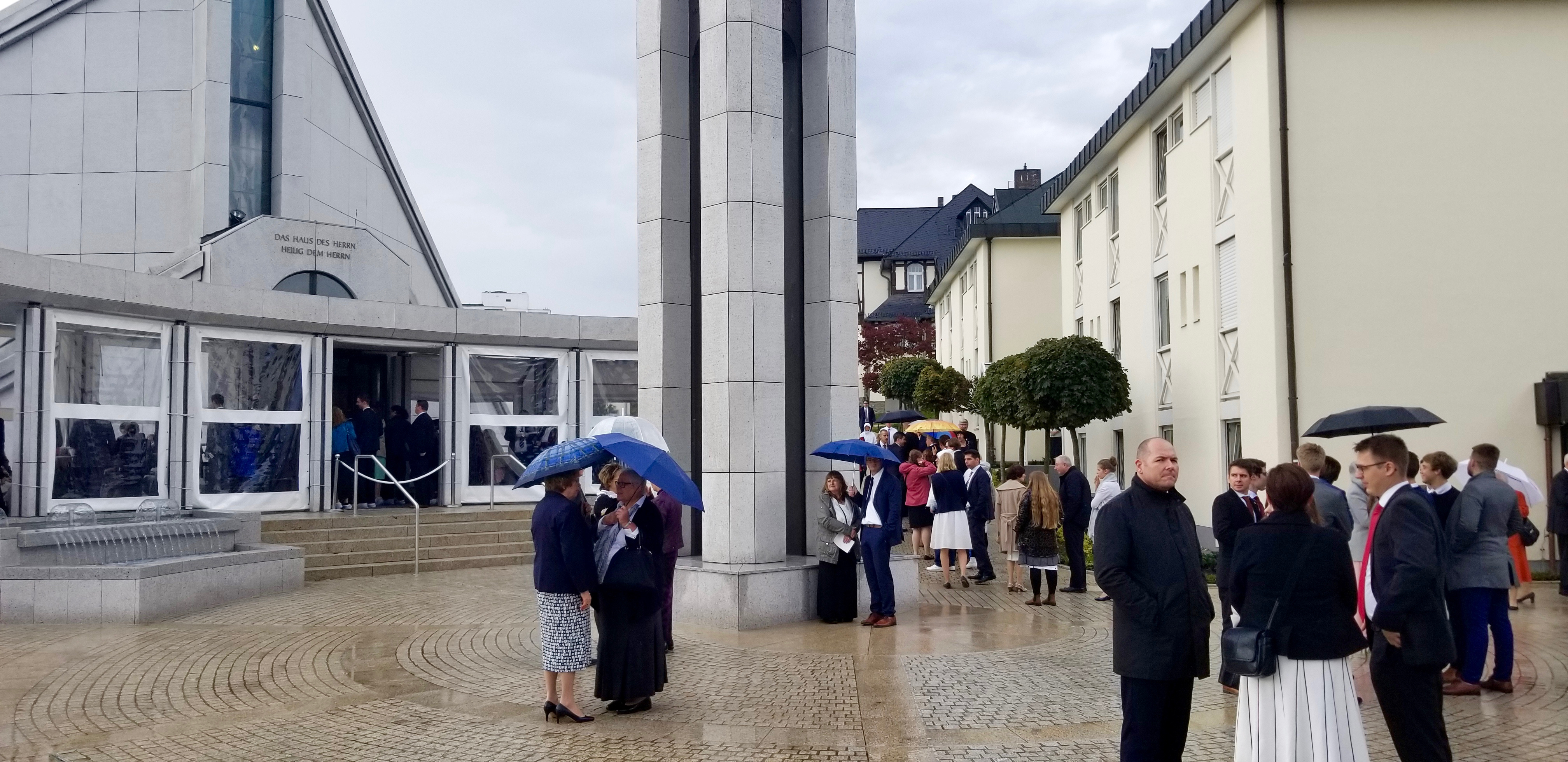 Individuals waiting outside the Frankfurt Germany Temple between rededication sessions on Sunday, Oct. 20, 2019, find cover under umbrellas from the drizzle.
