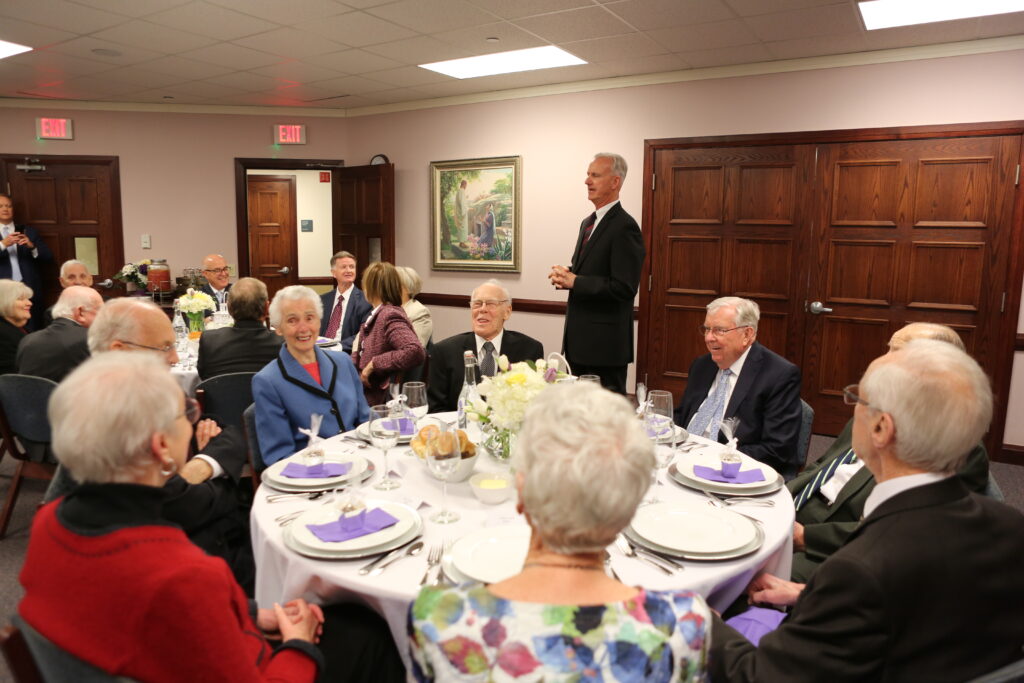 President M. Russell Ballard, acting president of the Quorum of the Twelve Apostles, has dinner with old friends as Michael Finnigan addresses the dinner audience at the Brampton Stake Center in Brampton, Ontario, Canada, March 6, 2020.