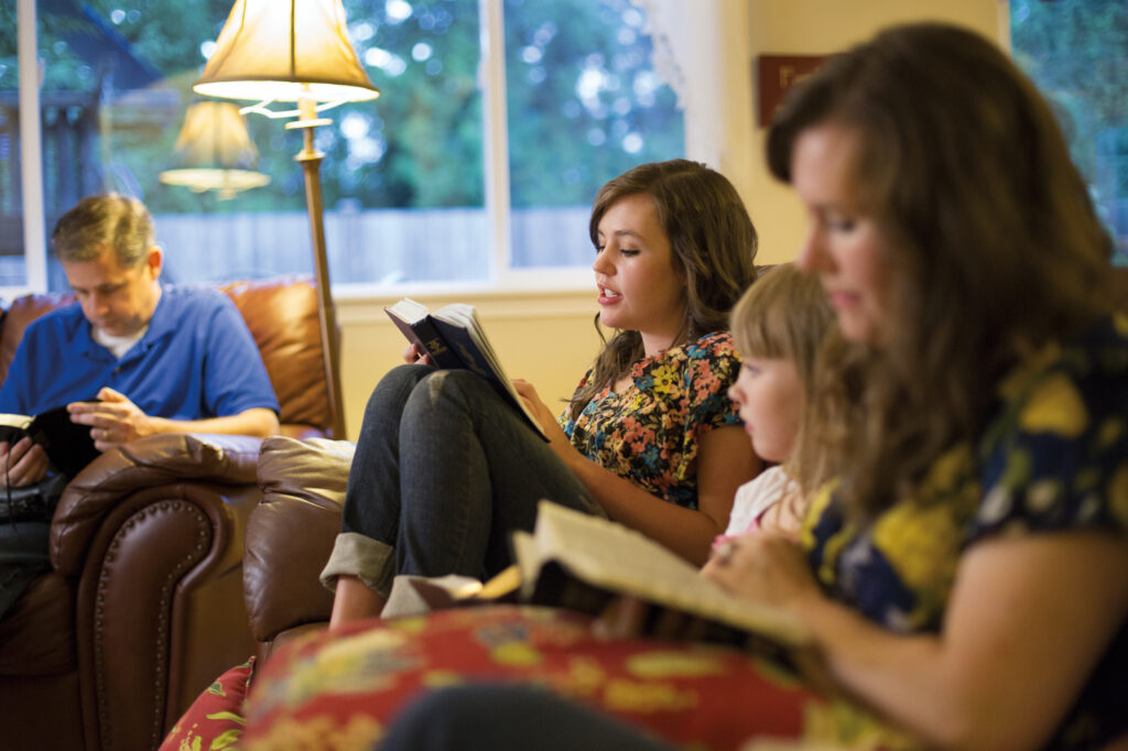 Uma jovem lê o Livro de Mórmon enquanto sua família acompanha sua leitura.