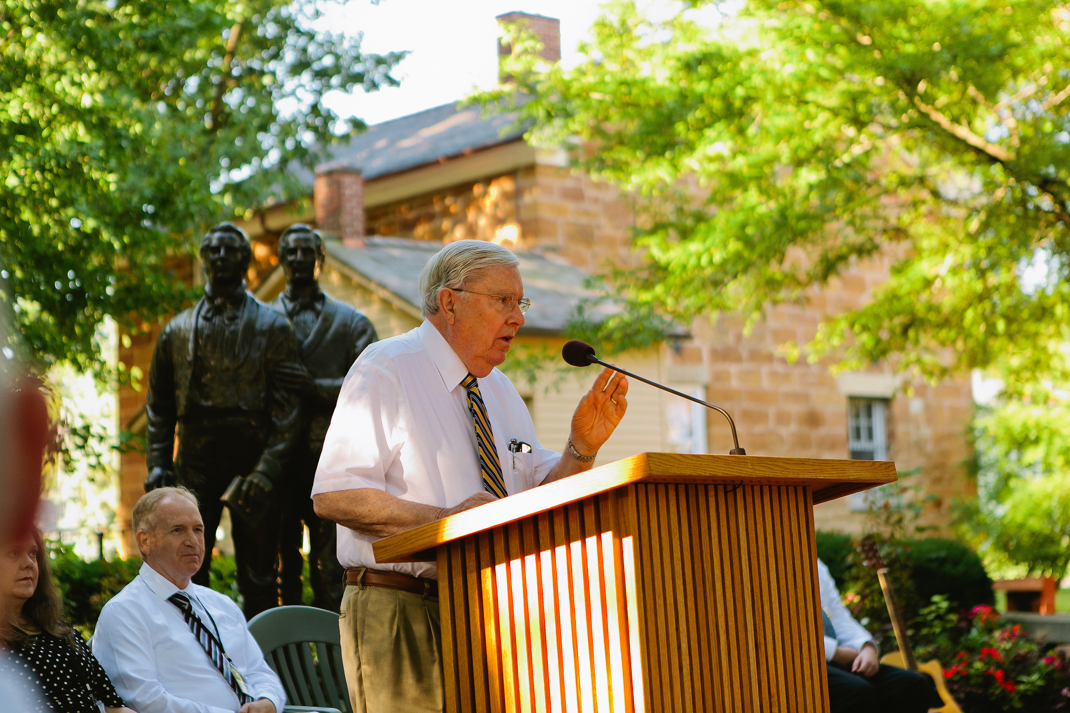 El élder M. Russell Ballard discursa en un devocional que se lleva a cabo afuera de la cárcel de Carthage el 5 de ago. El devocional conmemoró el aniversario número 25 de la dedicación del cementerio de la familia Smith.