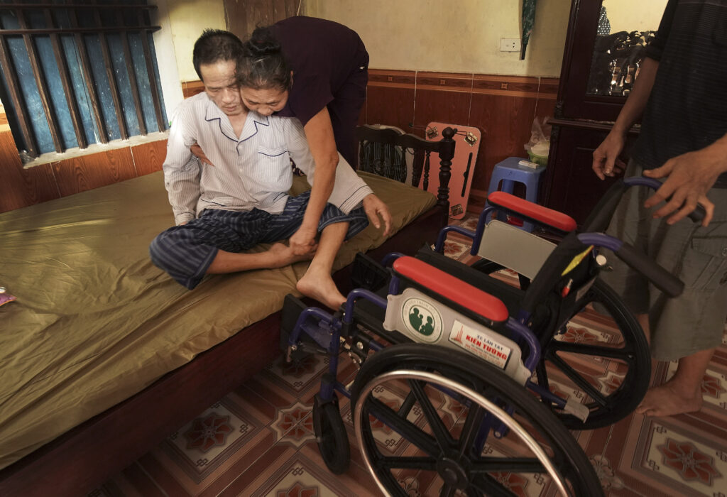Bao Dinh Tran es ayudado por su esposa Quyen Thi Mai a subir a su silla de ruedas que recibió de Latter-day Saints Charities en Hanói, Vietnam, el sábado, 16 de noviembre de 2019.